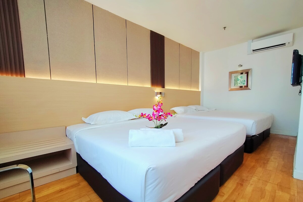 A hotel room with two beds, a wooden floor, a wall-mounted air conditioner, and a small picture frame.