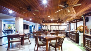 Un restaurant spacieux avec des tables et des chaises en bois, des ventilateurs de plafond et une vue sur l’espace extérieur.