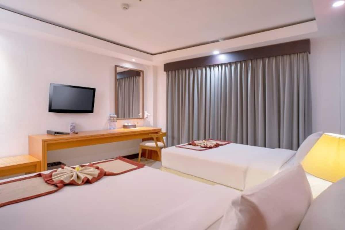 A hotel room with two beds, a desk, a television, and a large window with curtains.