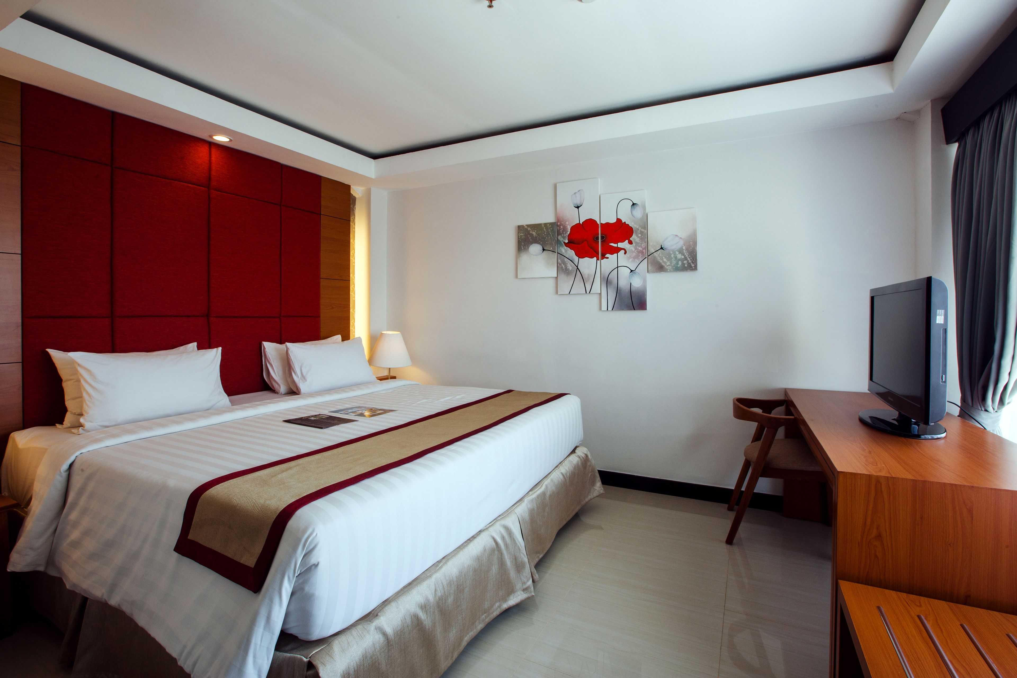 A hotel room with a large bed, a desk with a television, and a wall-mounted artwork.