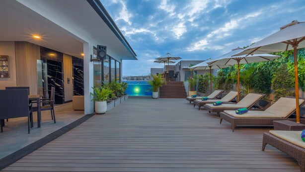Une terrasse sur le toit avec des chaises longues et des parasols, une piscine en arrière-plan et une façade d’immeuble moderne.