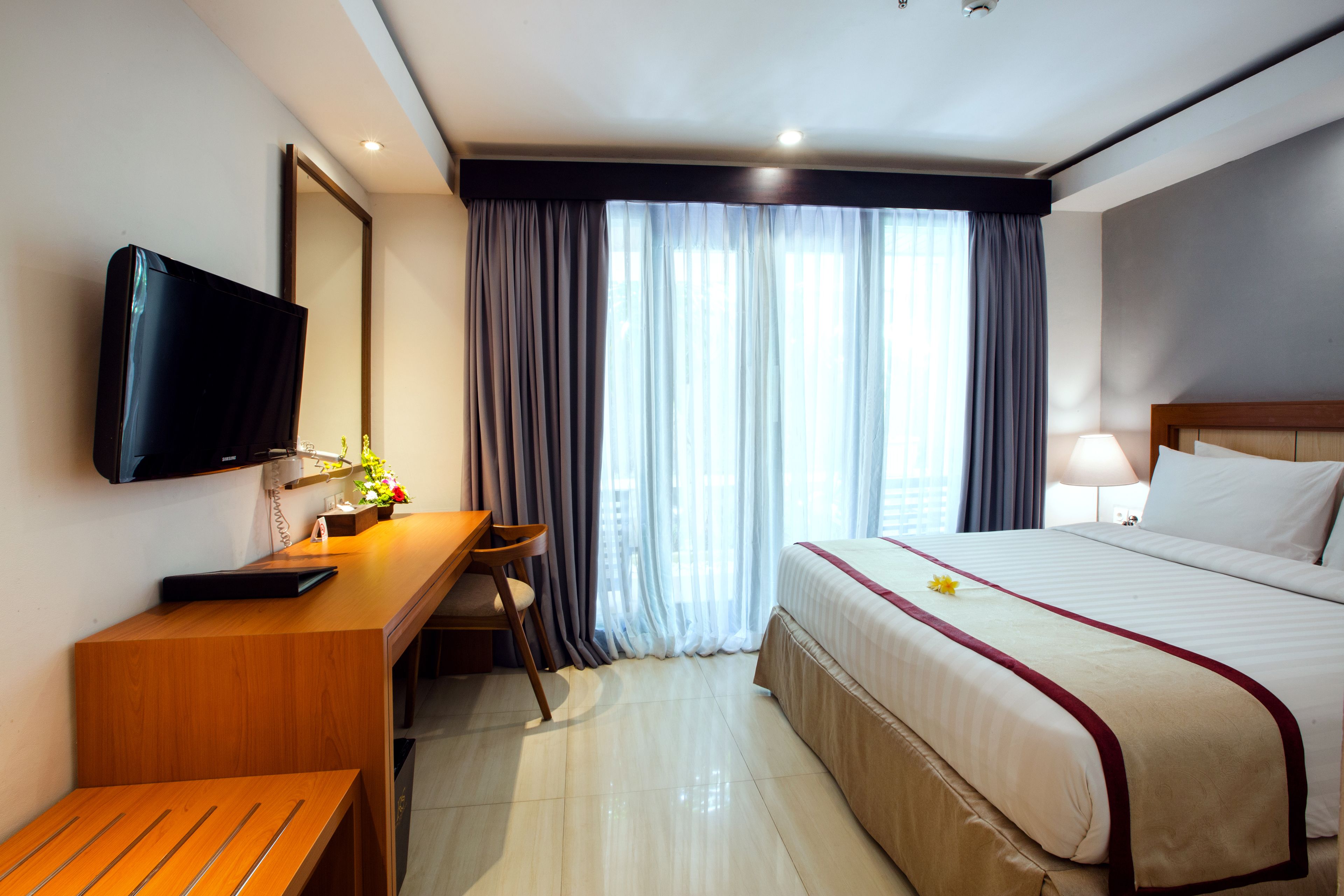 Une chambre d’hôtel équipée d’un lit, d’un bureau, d’une chaise, d’une télévision et de rideaux.