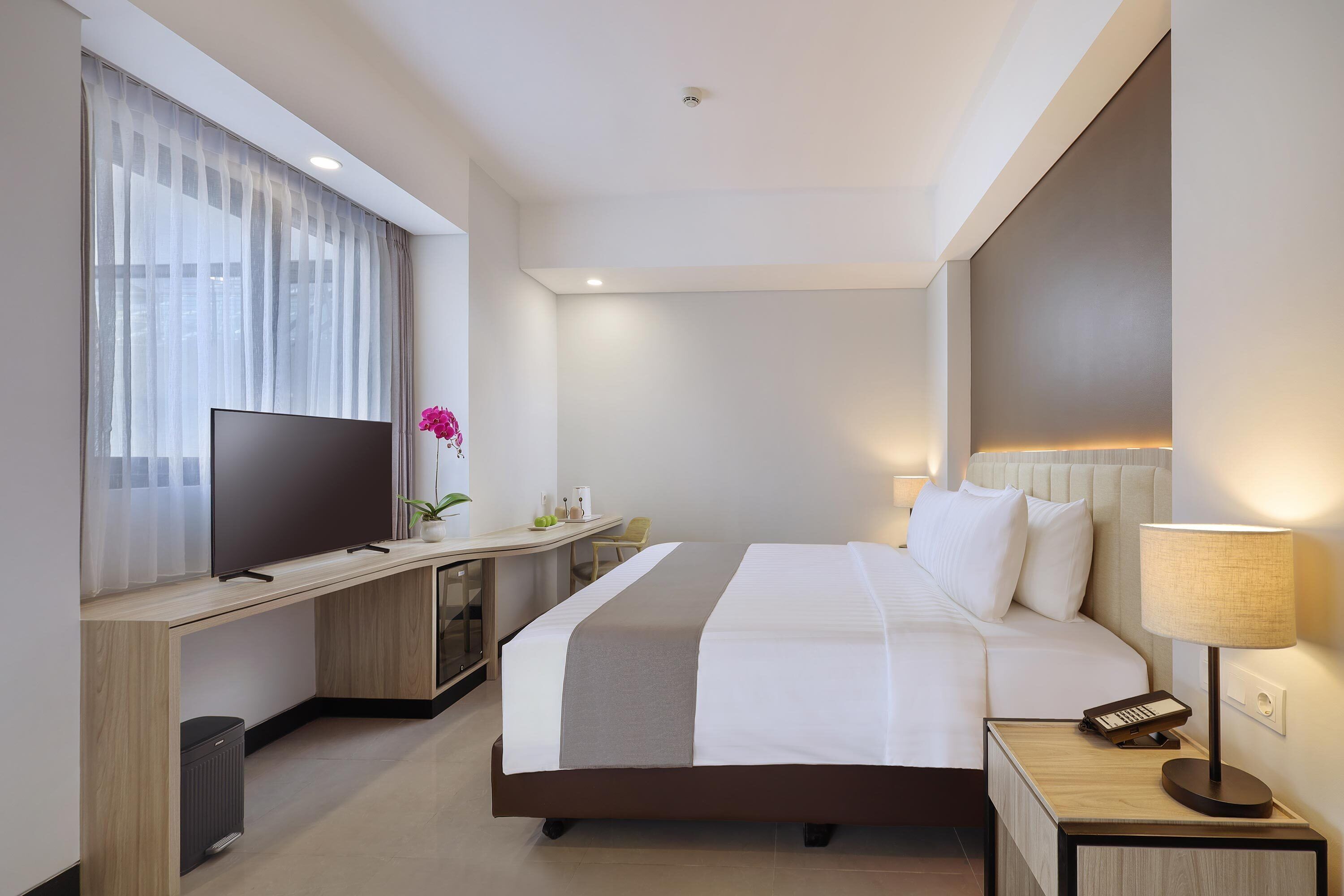 Ein modernes Hotelzimmer mit einem großen Bett, einem Fernseher, einem Schreibtisch und einer Lampe.