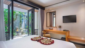 Une chambre d’hôtel équipée d’un lit, d’un bureau, d’une chaise, d’une télévision et offrant une vue sur un jardin grâce à une porte vitrée.