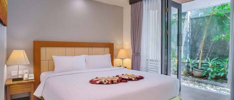 Habitación de hotel con una cama grande, lámparas de noche, un teléfono y vistas a un jardín a través de una puerta de cristal.