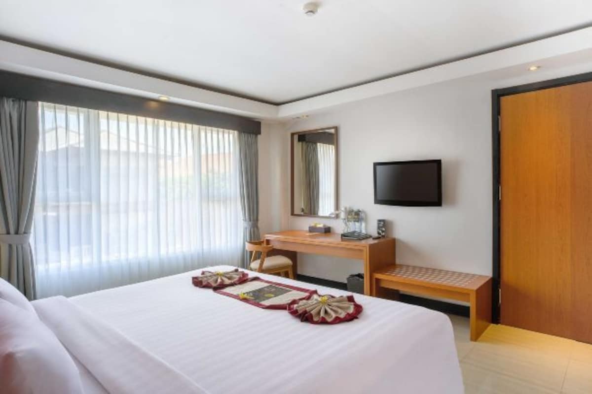 A hotel room with a bed, a desk, a chair, a TV, and a window with curtains.