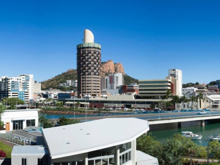A coastal cityscape with modern buildings, a prominent cylindrical structure, and a bridge over a body of water.