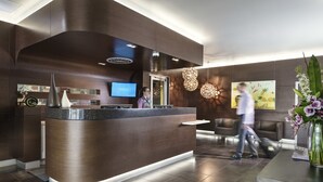 A modern reception area with a curved counter, a flat-screen TV, and a decorative wall with a painting. - Grand Hotel and Apartments Townsville (South Townsville)