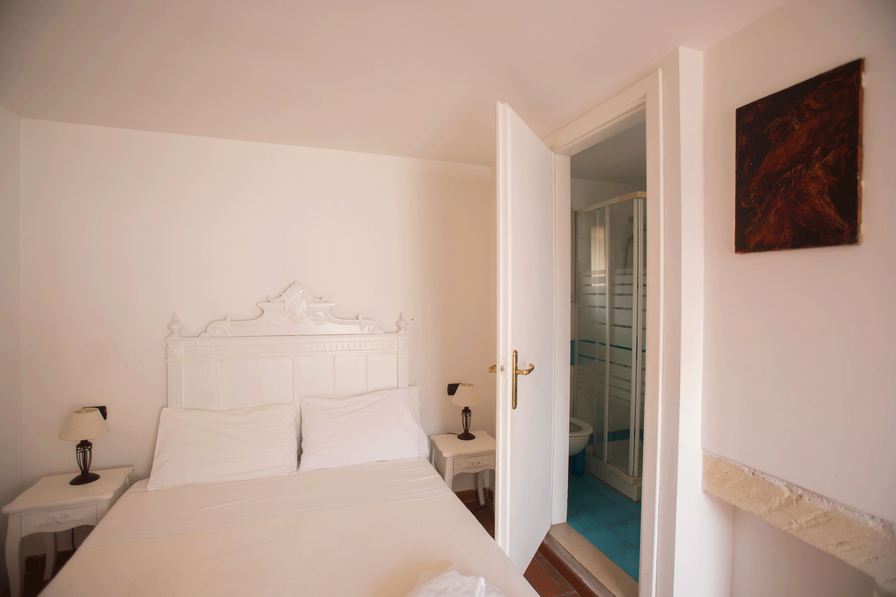 Un dormitorio blanco con una cama, mesitas de noche y una puerta que da a un baño.
