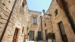 A narrow stone courtyard with a central door, flanked by buildings with windows and doors, and a street lamp.