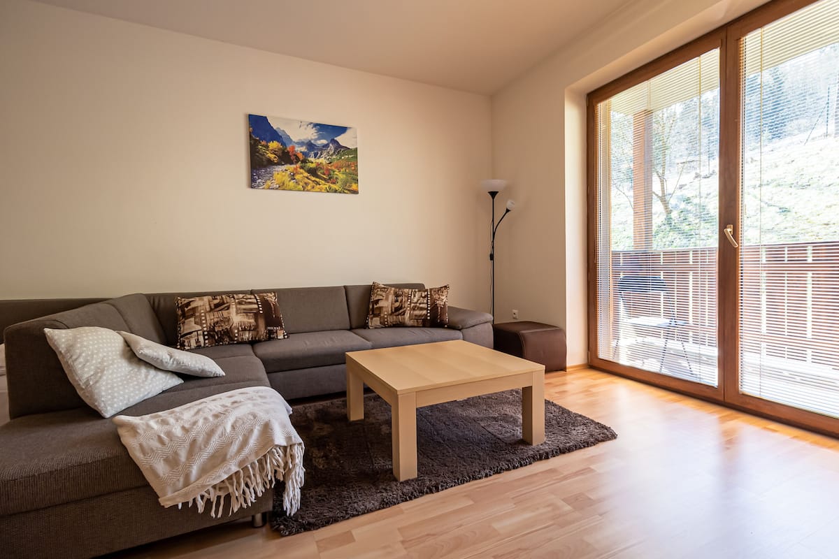 A modern living room with a sofa, a wooden coffee table, and a large window with blinds.