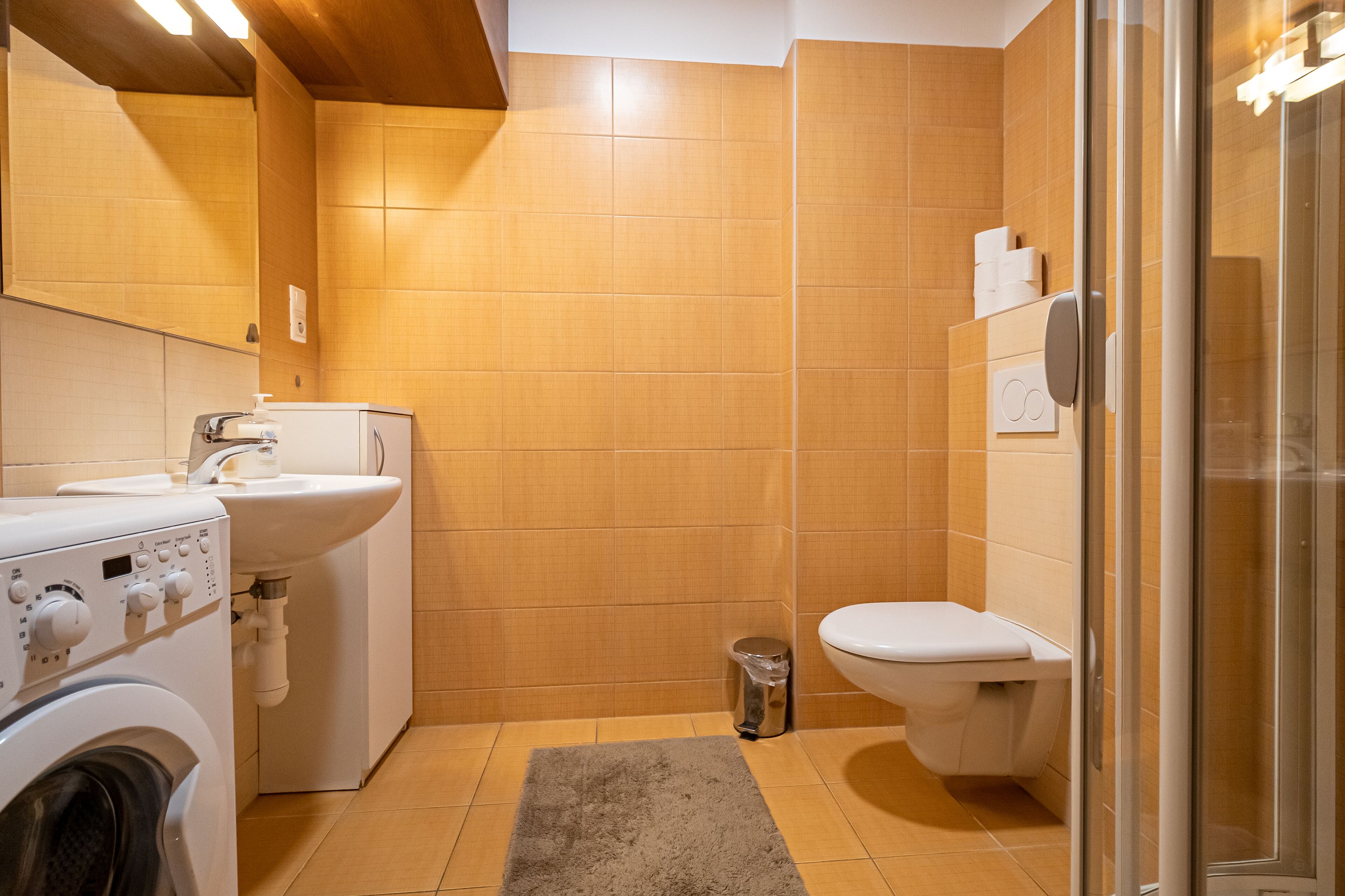 Ein modernes Badezimmer mit Waschmaschine, Waschbecken, Toilette und Duschkabine aus Glas.