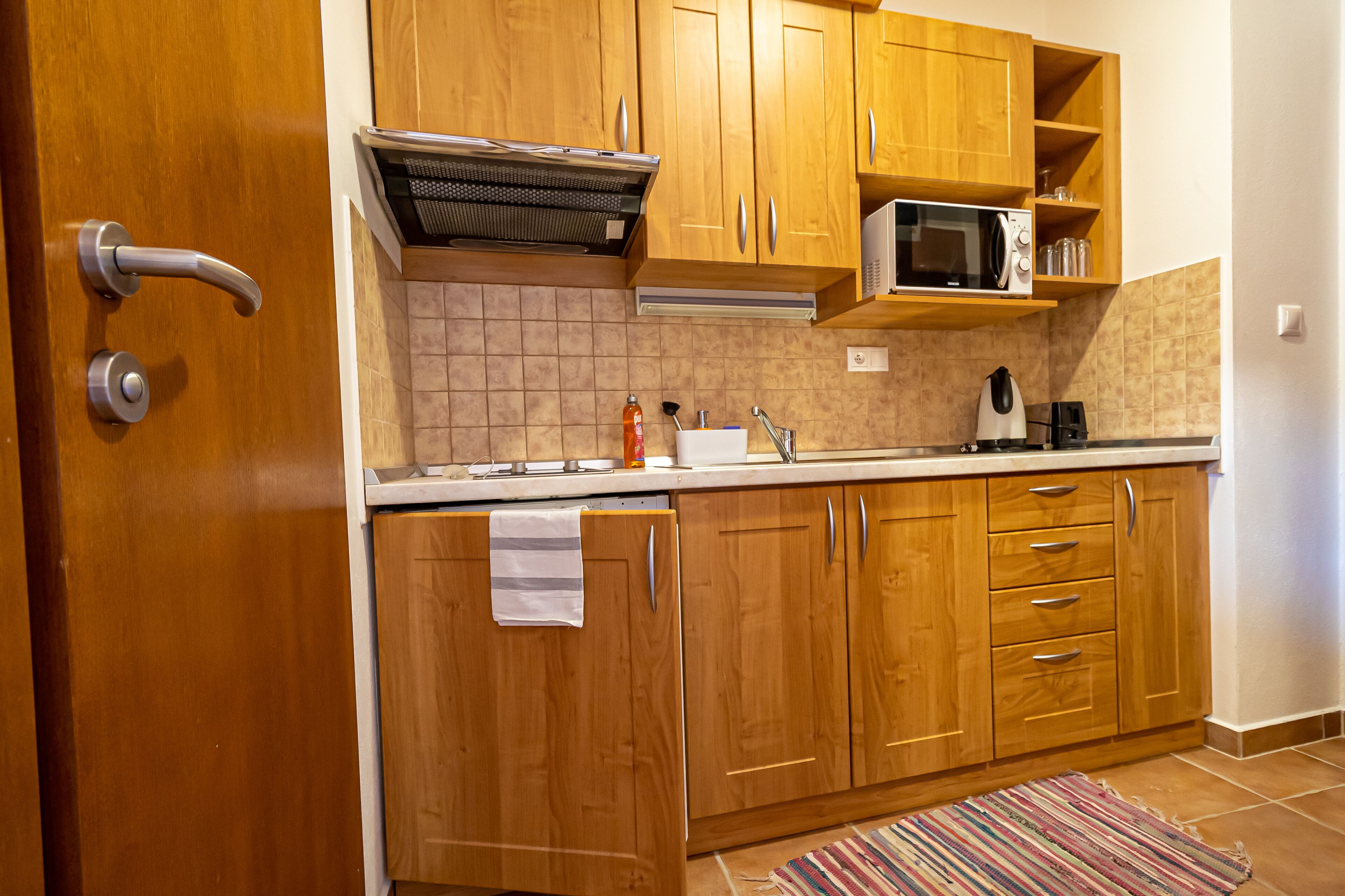 A kitchen with wooden cabinets, a microwave, a kettle, and a tiled backsplash.