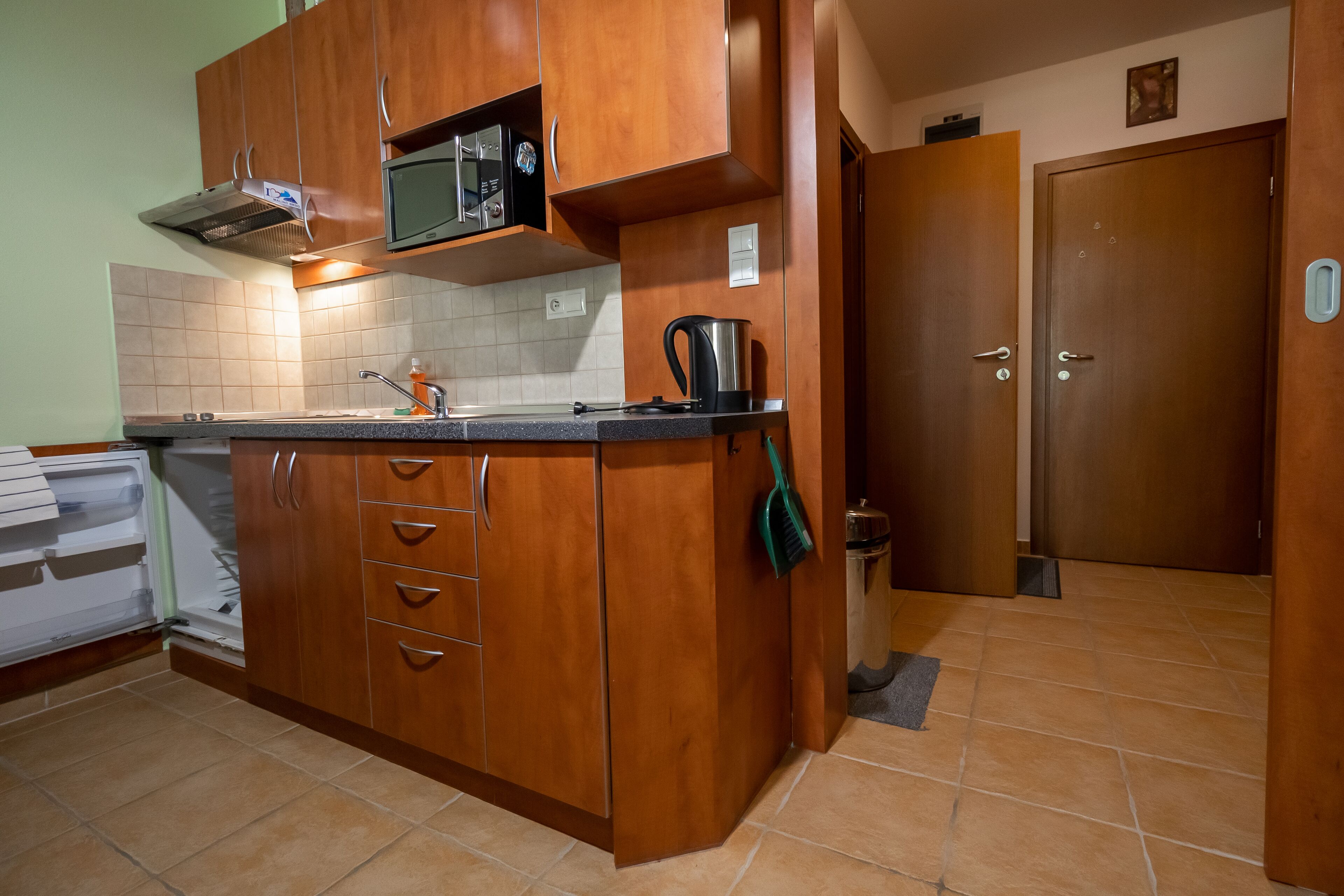 A kitchen with wooden cabinets, a microwave, a kettle, and a sink.