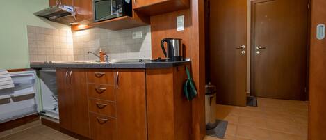 A kitchen with wooden cabinets, a microwave, a kettle, and a sink.