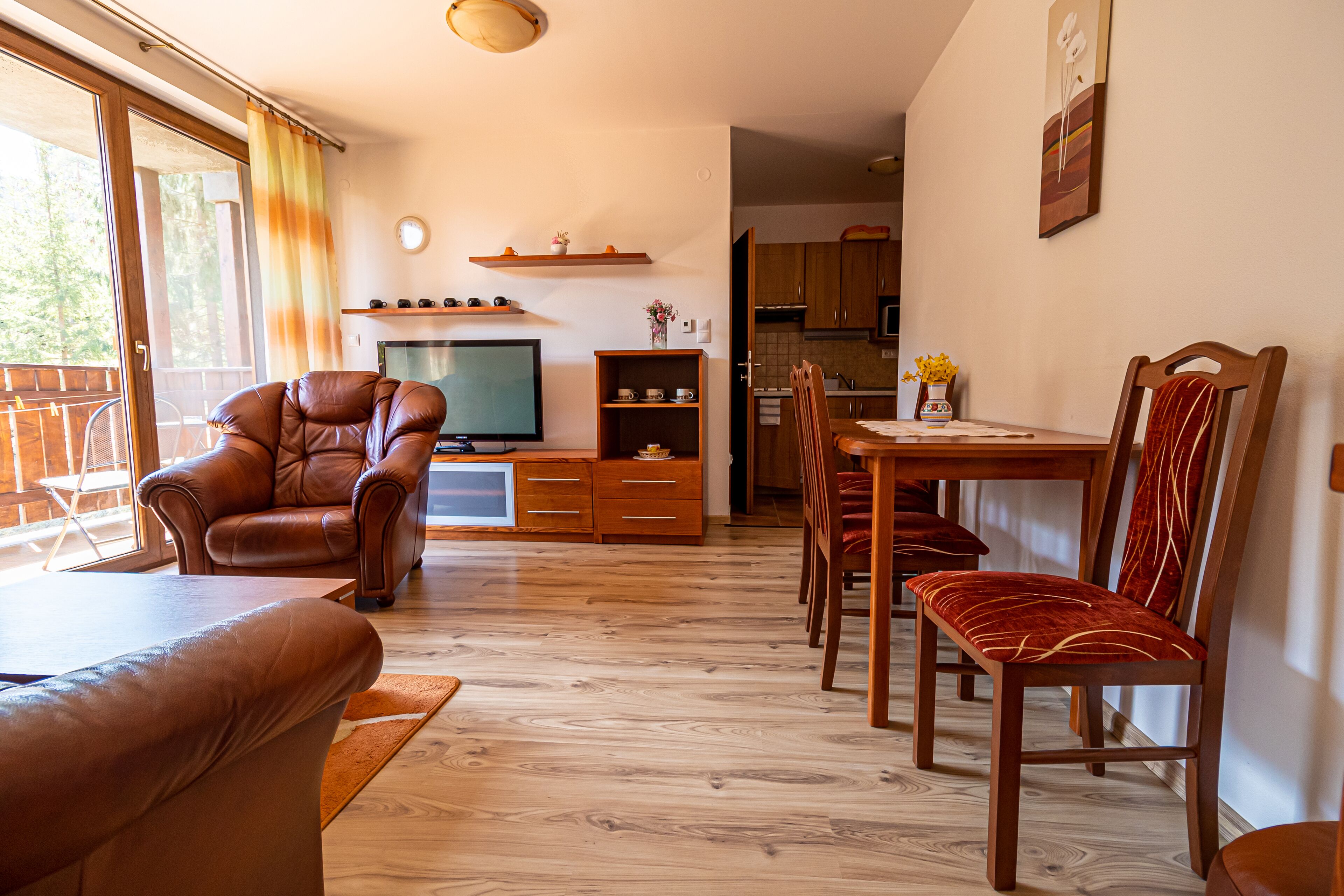 Ein Wohnzimmer mit Ledersofa, Fernseher, Holzschränken und einem Essbereich mit Tisch und Stühlen.