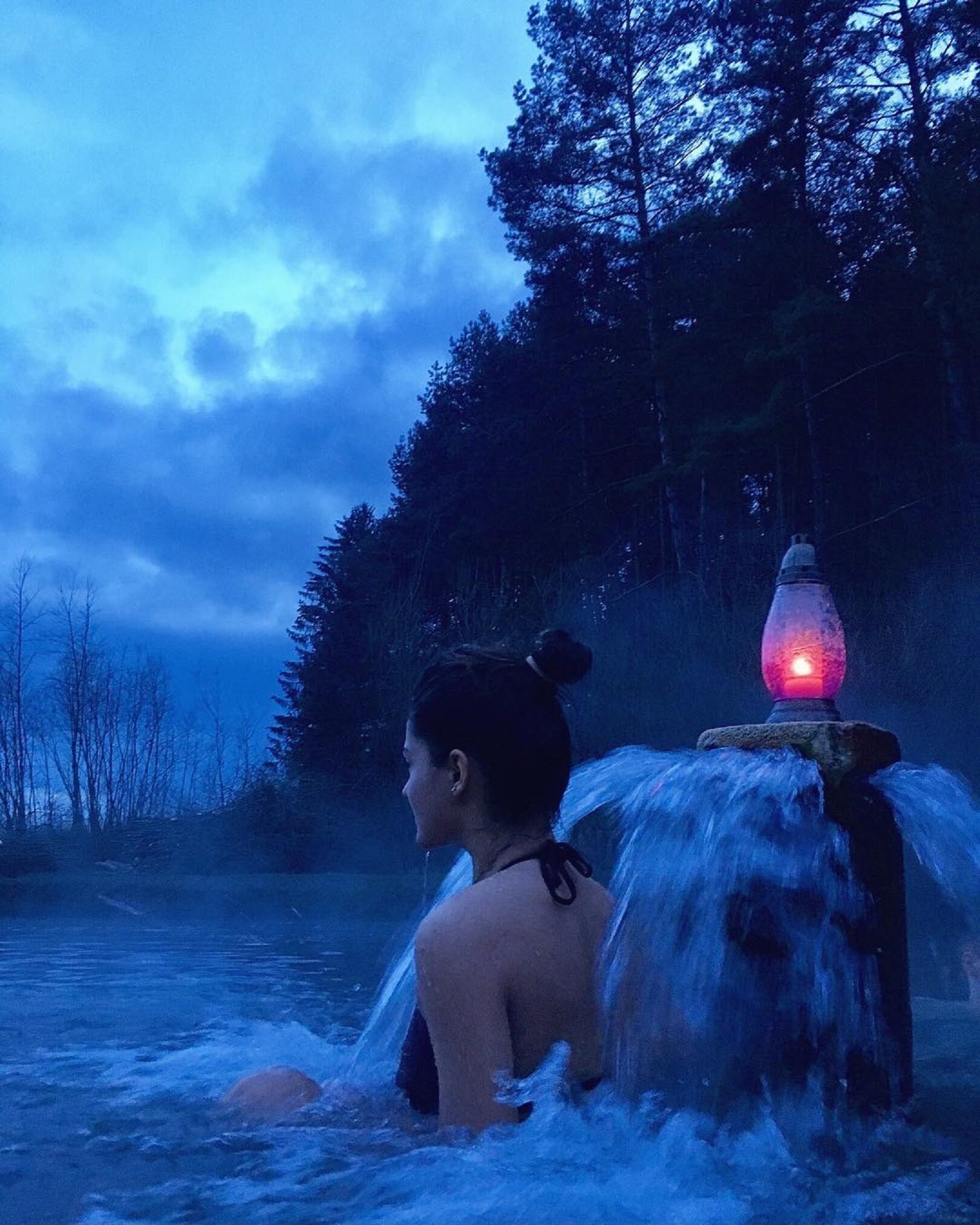 A person in a natural setting with a body of water and trees in the background.