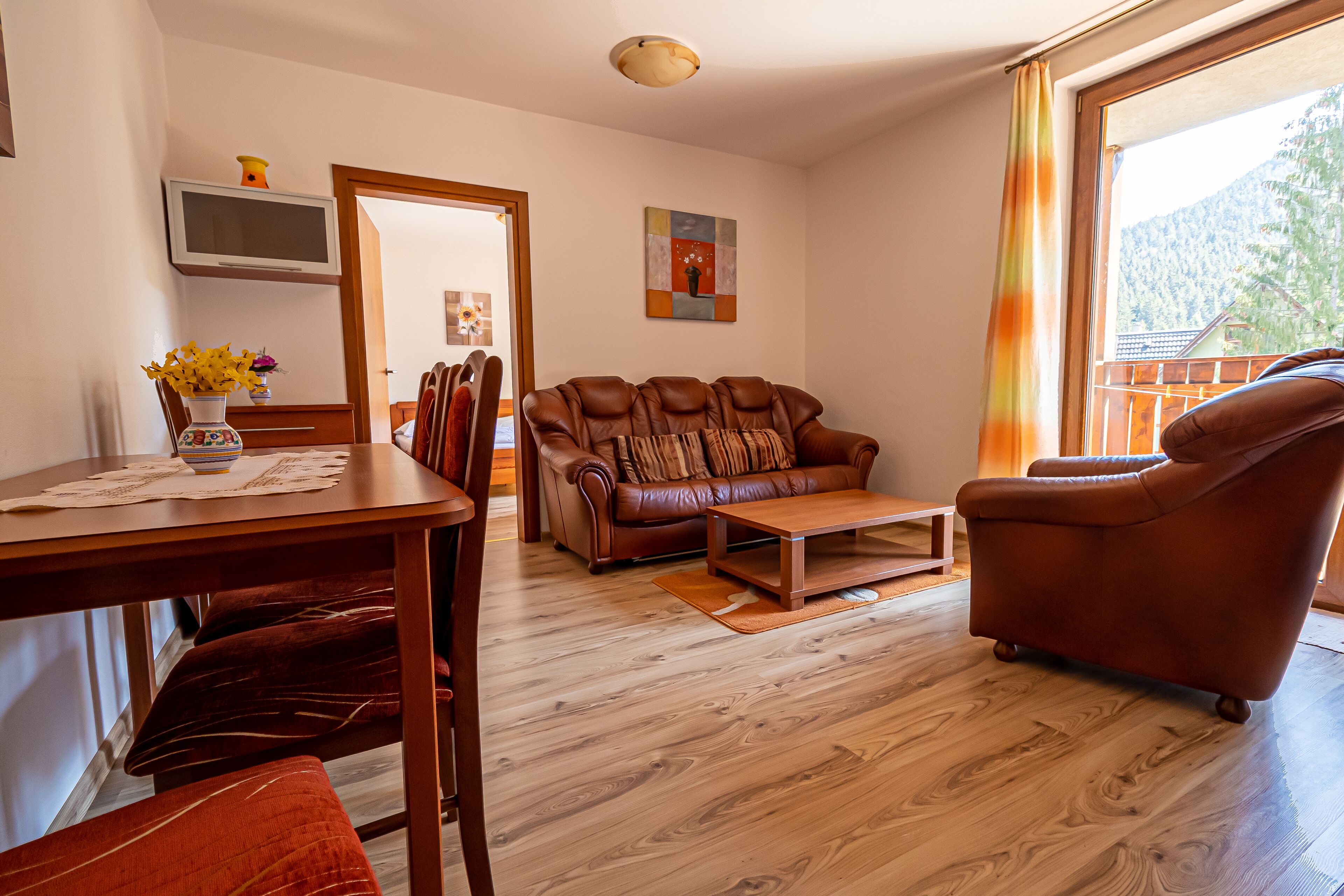 Una sala de estar con un sofá de cuero marrón, una mesa de centro de madera y una mesa de comedor con sillas.