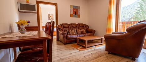 Una sala de estar con un sofá de cuero marrón, una mesa de centro de madera y una mesa de comedor con sillas.