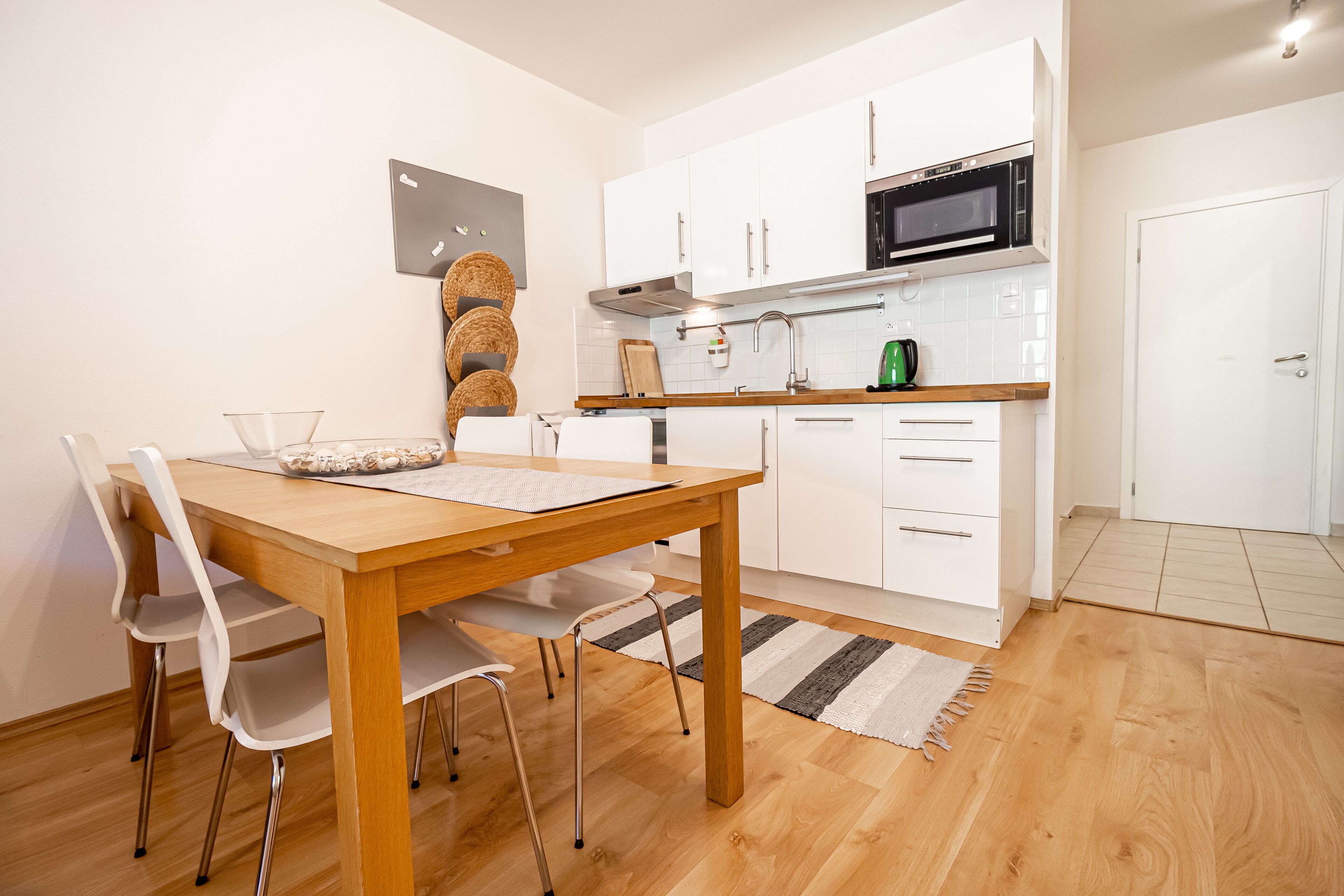 A modern kitchen with white cabinets, a wooden dining table, and a microwave.
