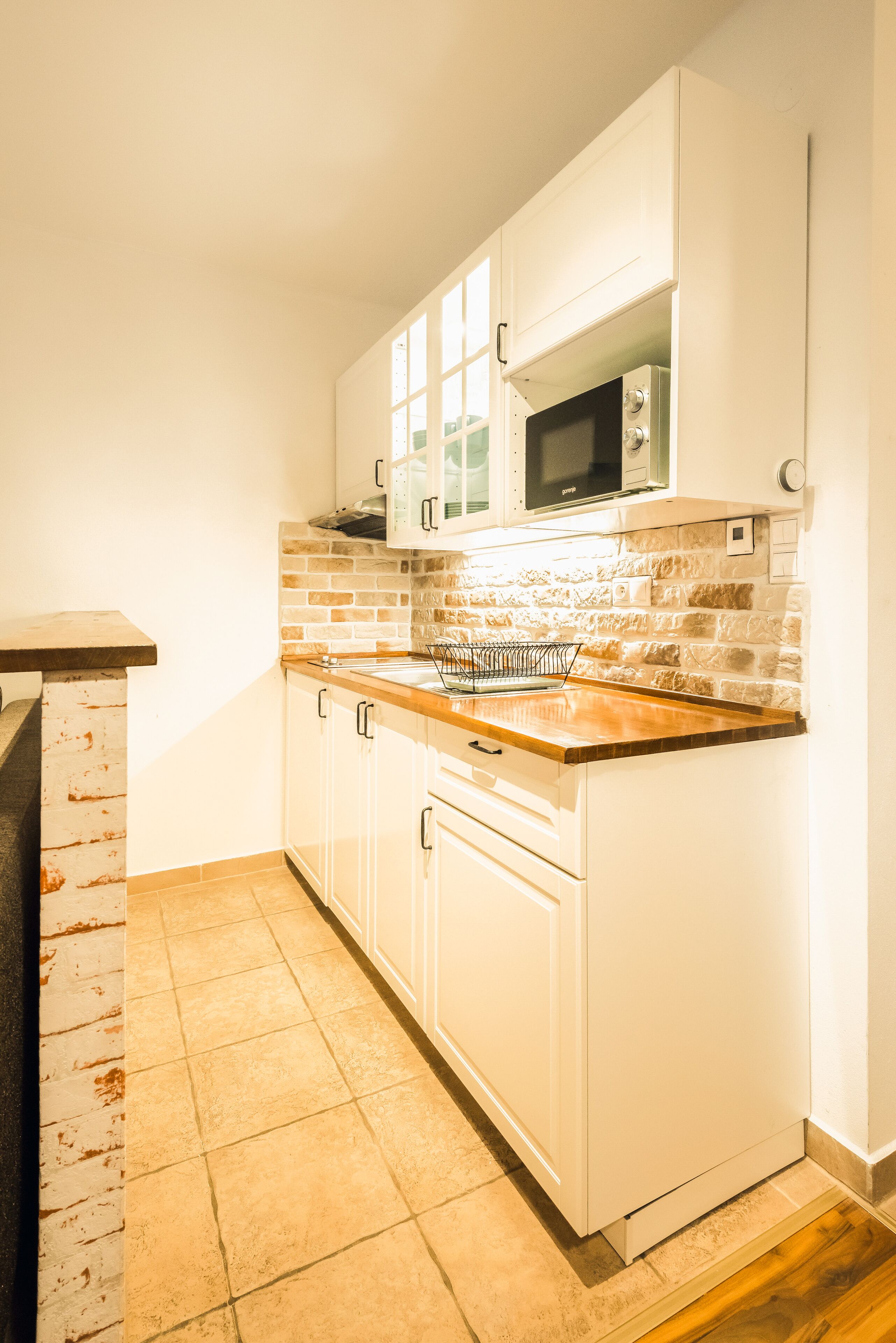 Una cocina con armarios blancos, salpicadero de ladrillo y encimera de madera.