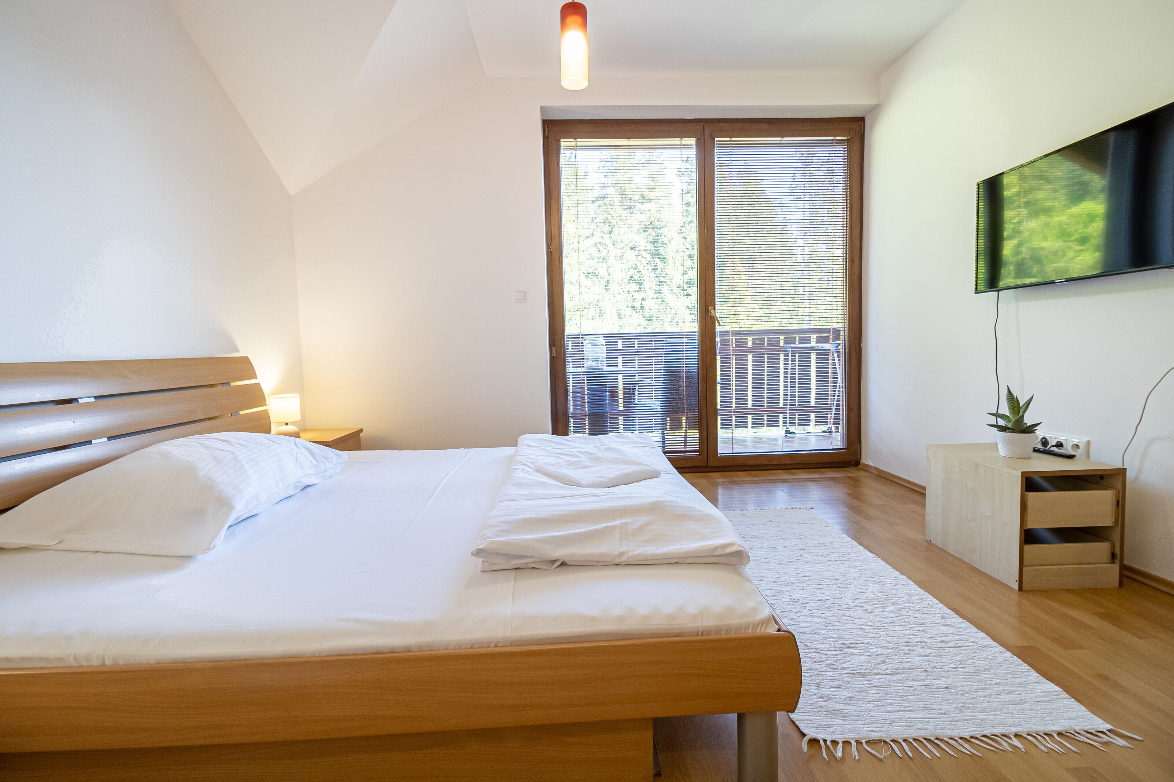 Quarto com cama, mesa de cabeceira e porta de vidro deslizante para uma varanda.