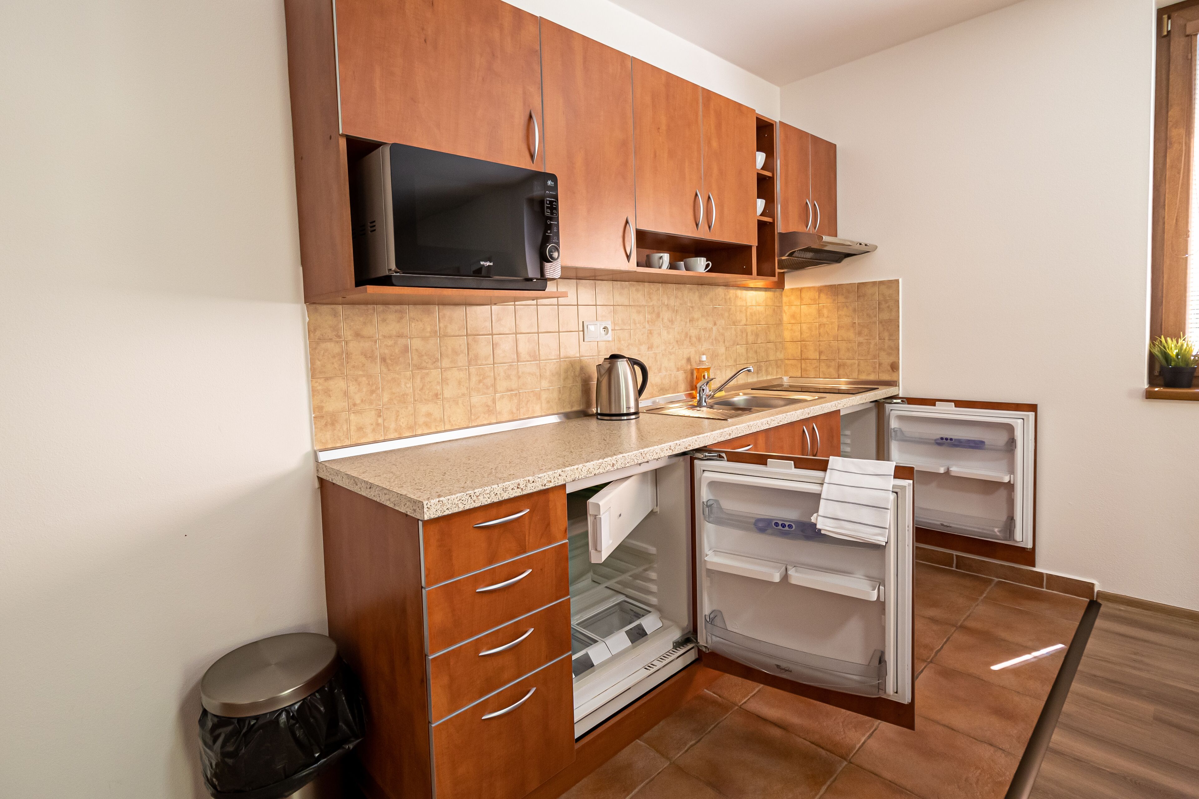 A compact kitchen with wooden cabinets, a microwave, a kettle, and a refrigerator.