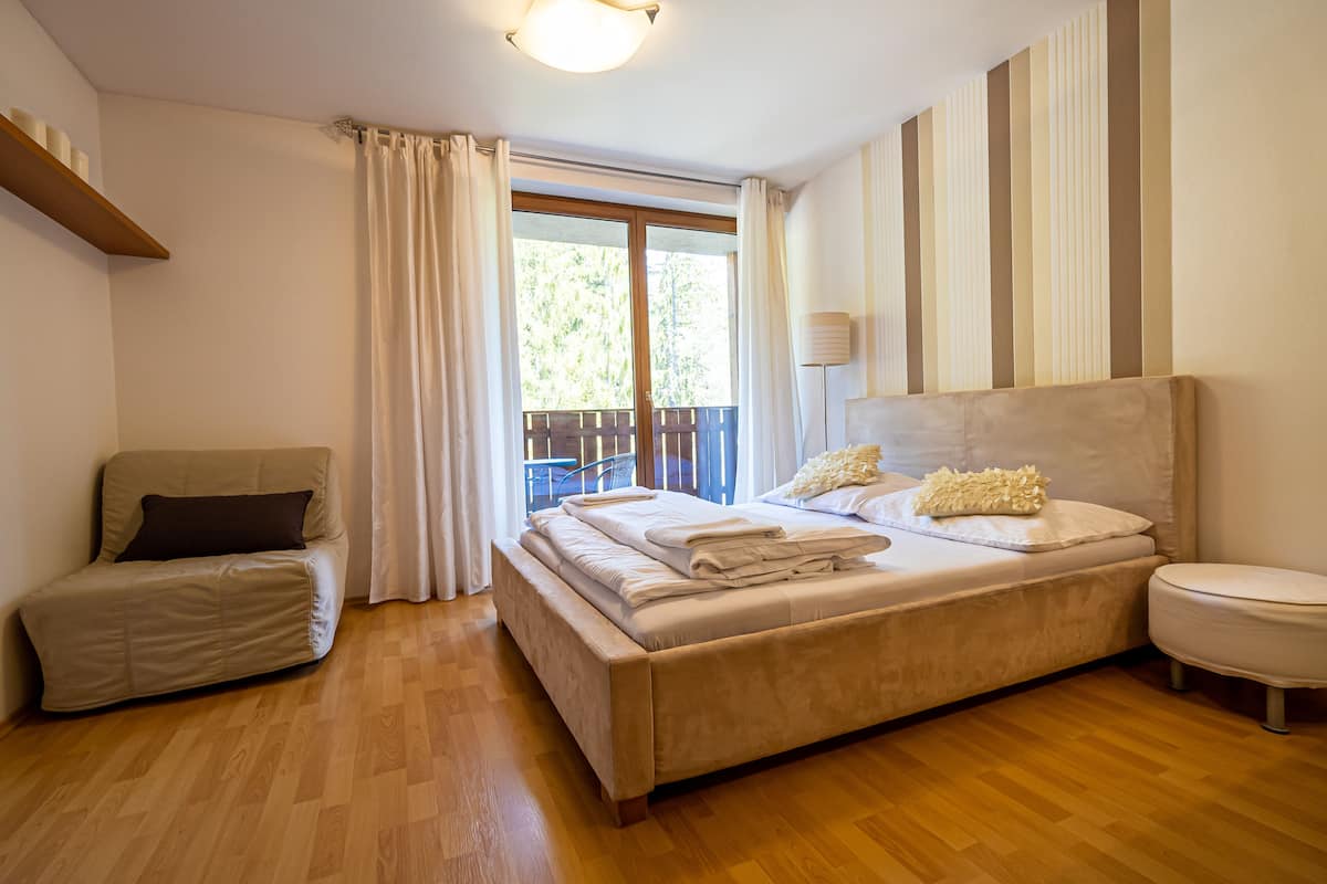A bedroom with a large bed, a sofa, a bedside table, and a window with curtains.
