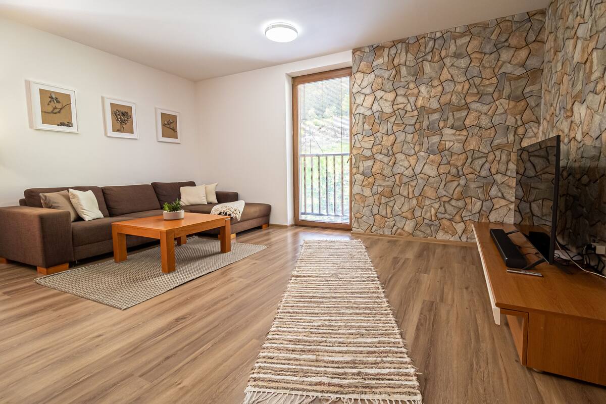 A living room with a brown sofa, a wooden coffee table, and a TV on a wooden stand.