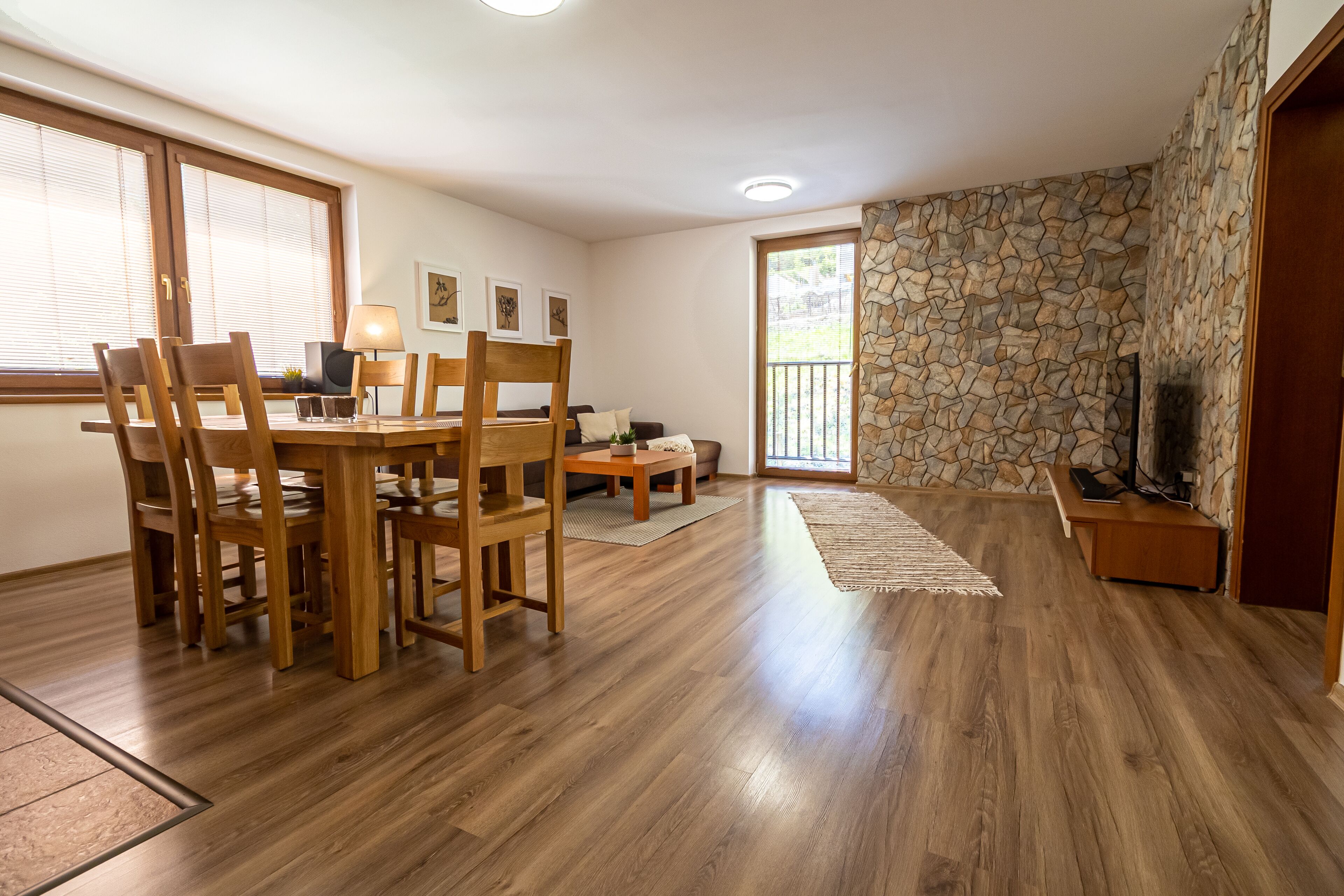 A dining area with wooden furniture, a stone wall, and a television on a wooden stand.
