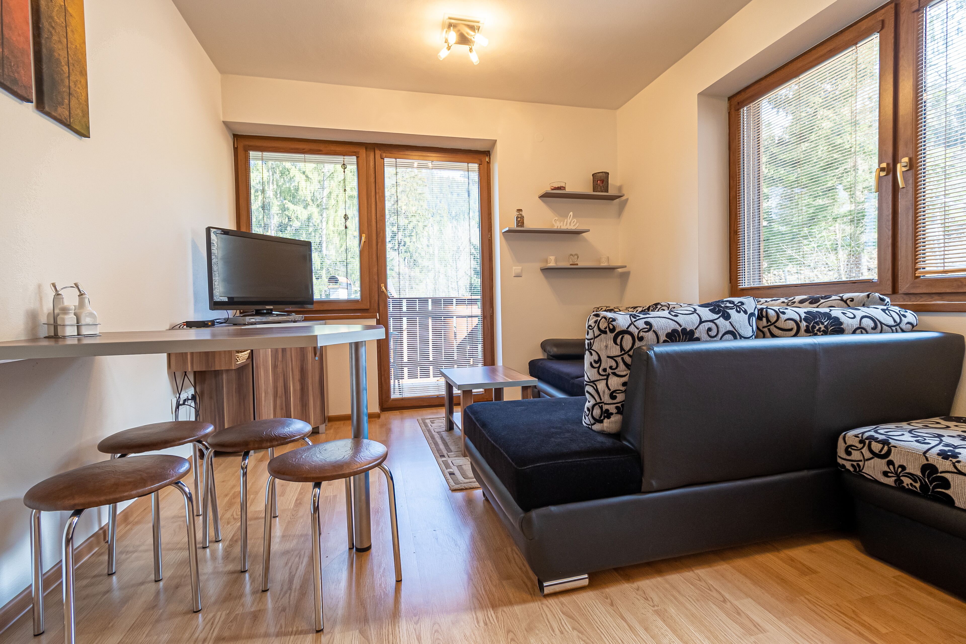 A modern living room with a sofa, a TV, and a dining area with stools.