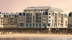 Un hotel frente a la playa con varios balcones, una playa arenosa en primer plano y un mar tranquilo.