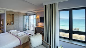 Habitación de hotel con dos camas, un escritorio y un amplio ventanal con vista al mar.