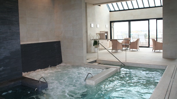 Un área interior de piscina moderna con hidromasaje, zona de estar y amplias ventanas con vistas.
