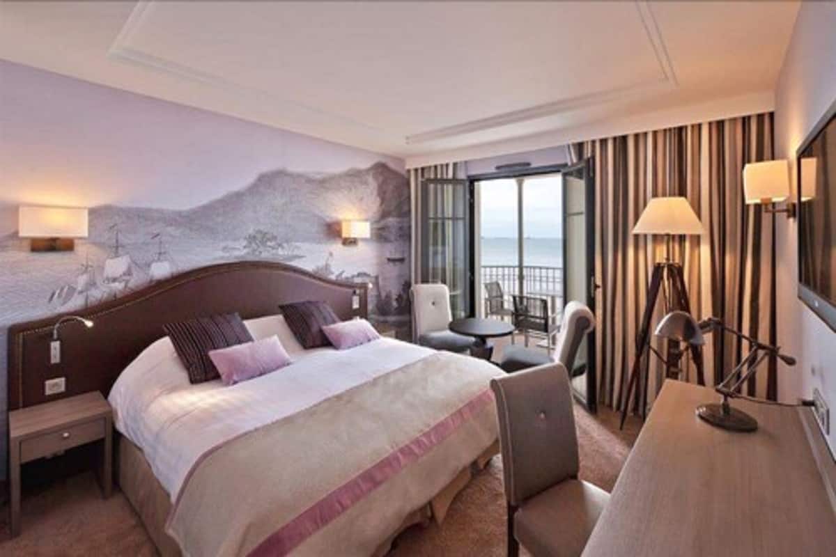A hotel room with a large bed, a desk, a chair, and a view of the sea.
