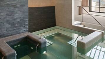A modern bathroom with a glass-enclosed hot tub, a wooden bench, and a view of the city through large windows.