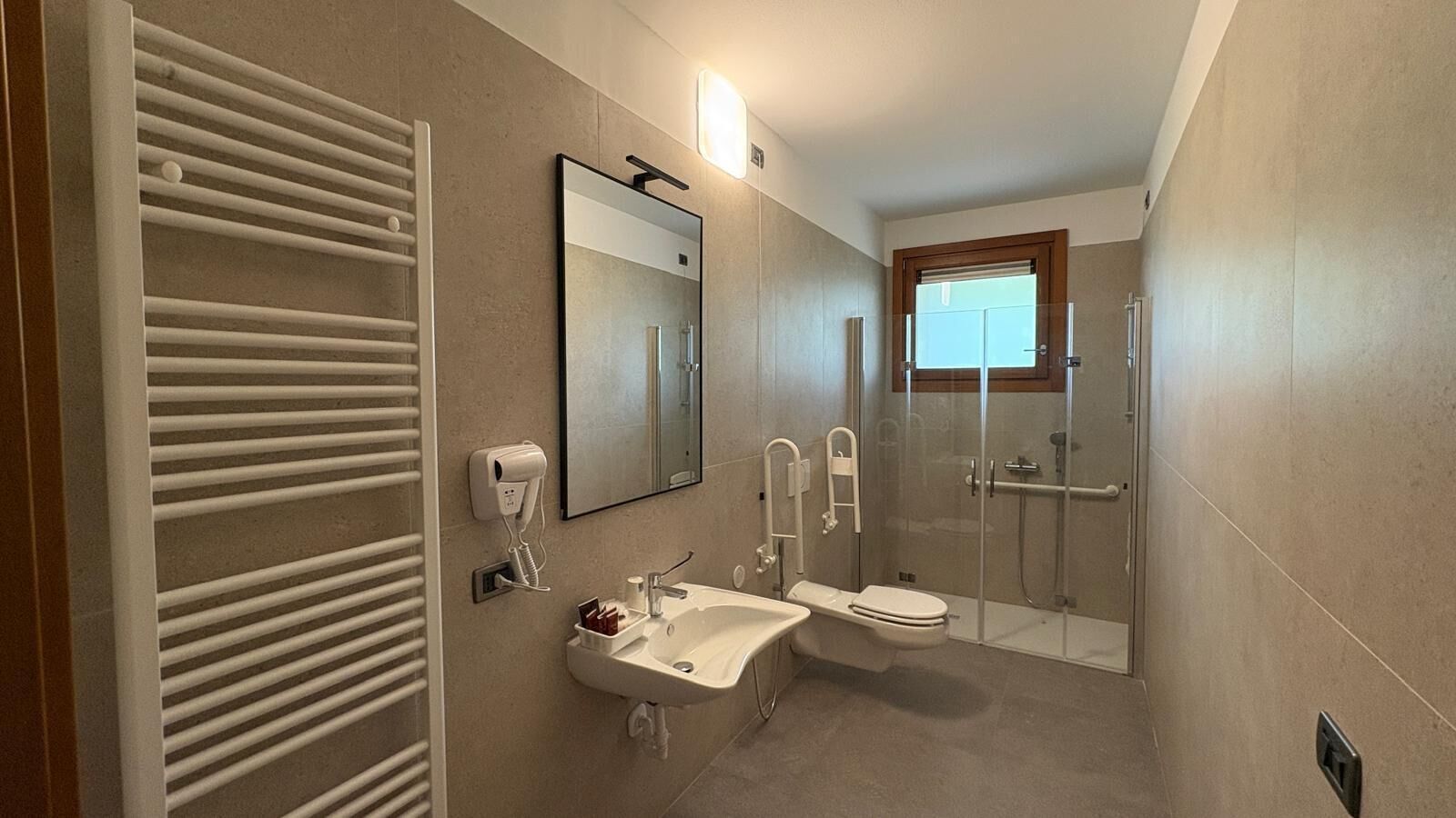 A bathroom with a toilet, sink, mirror, towel rack, and a glass-enclosed shower.