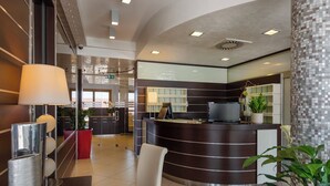 Una recepción moderna con un mostrador curvo, un espacio de espera con una silla blanca y una planta en maceta.