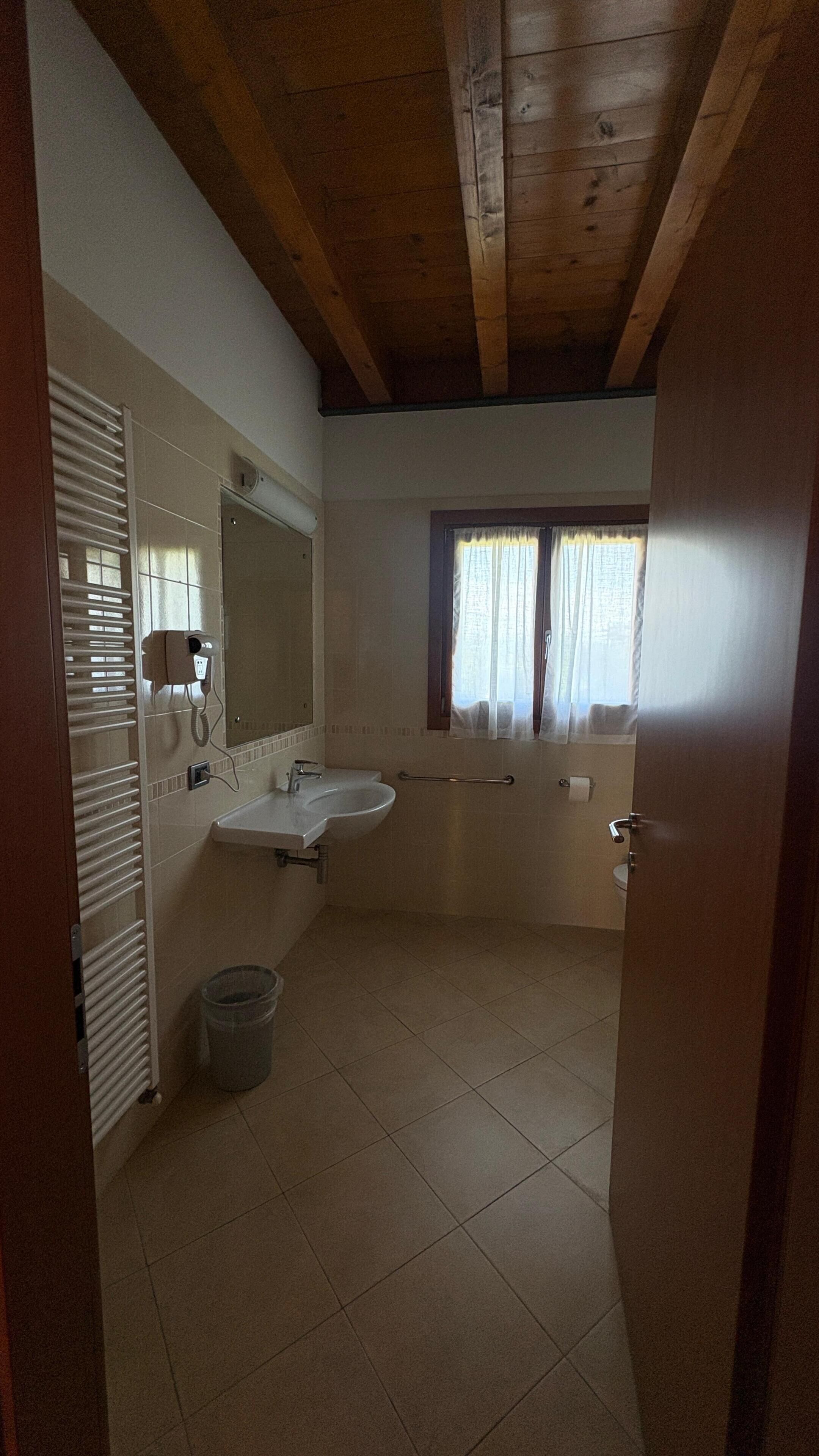 Un baño con lavamanos, espejo, ventana y un perchero para toallas.