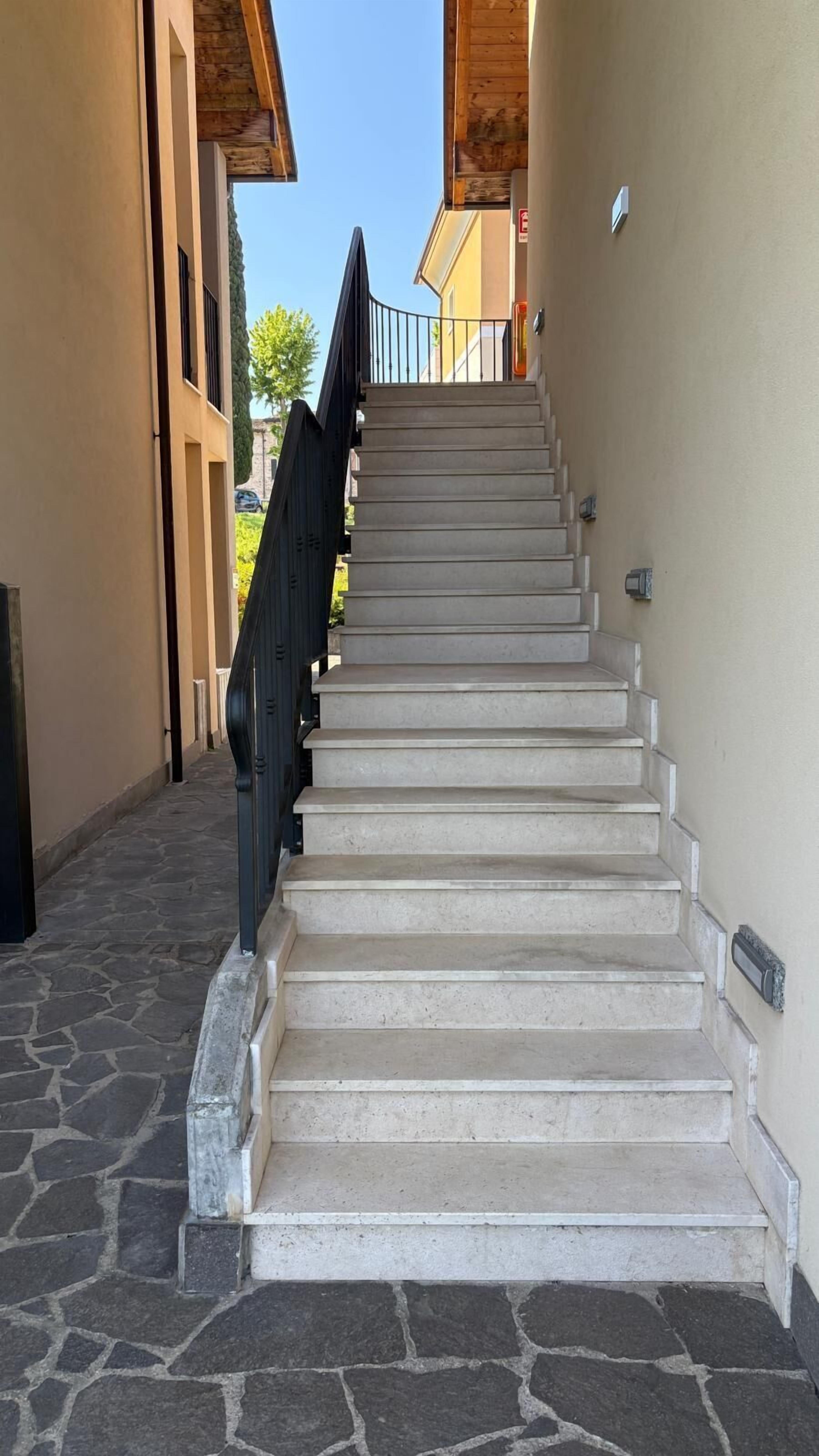 Un escalier menant à l’entrée d’un bâtiment, avec des marches en pierre et une rampe métallique.