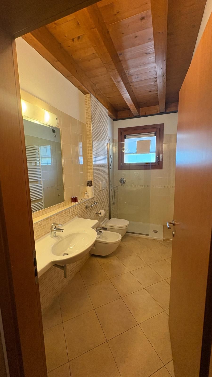 Un baño con techo de madera, un espejo grande, un lavamanos, un inodoro y una ducha.