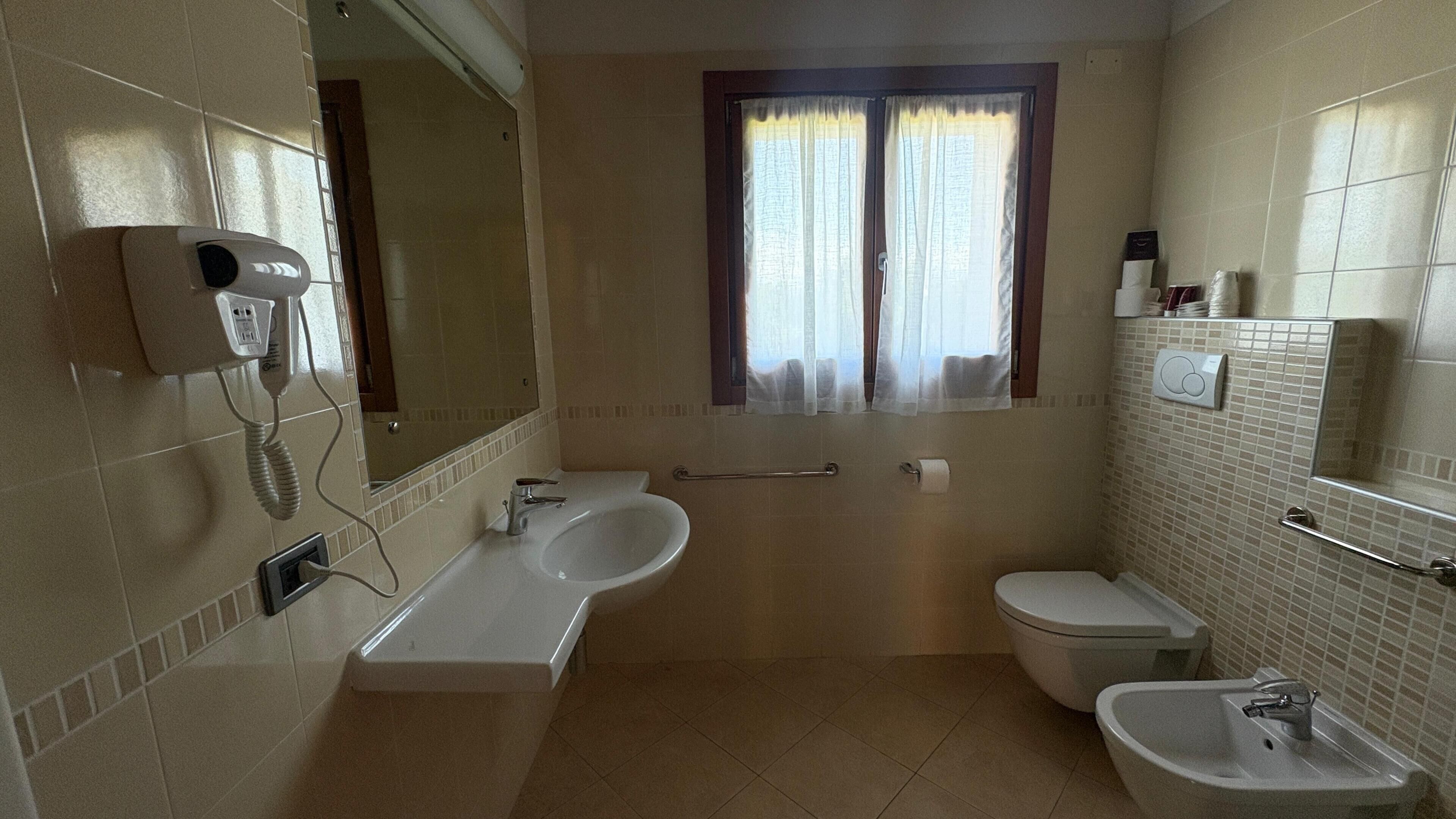 A bathroom with a bathtub, a sink, and a toilet. There is a window with curtains, a mirror, and a telephone mounted on the wall.