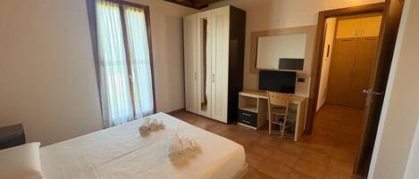 Un dormitorio con cama, escritorio, silla, armario y espejo.