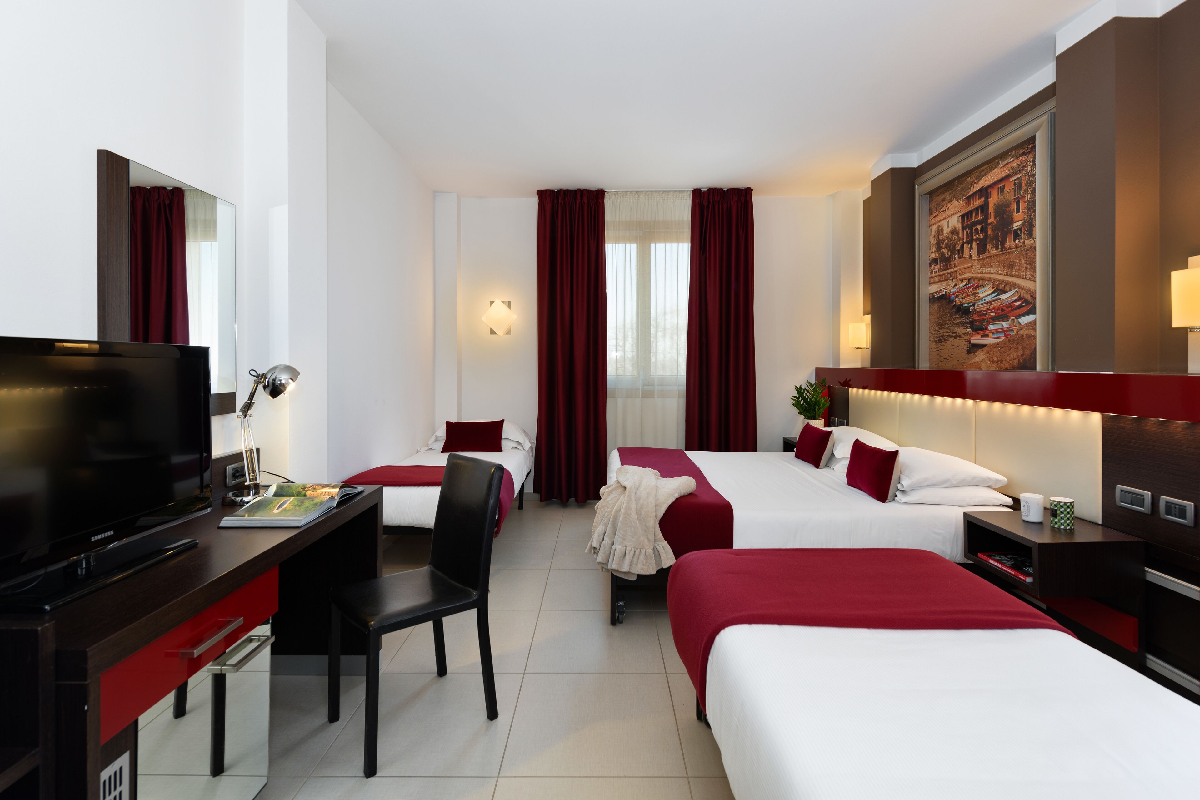 Habitación de hotel con televisión, escritorio, dos camas y un cuadro grande en la pared.