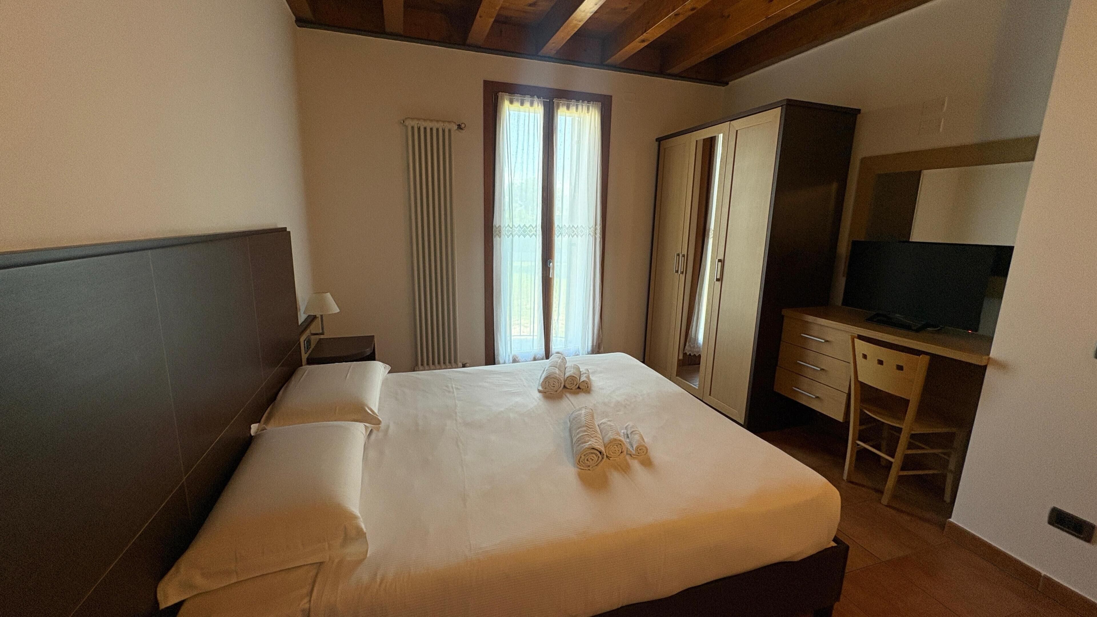 Een slaapkamer met een bed, een bureau, een televisie en een kledingkast.