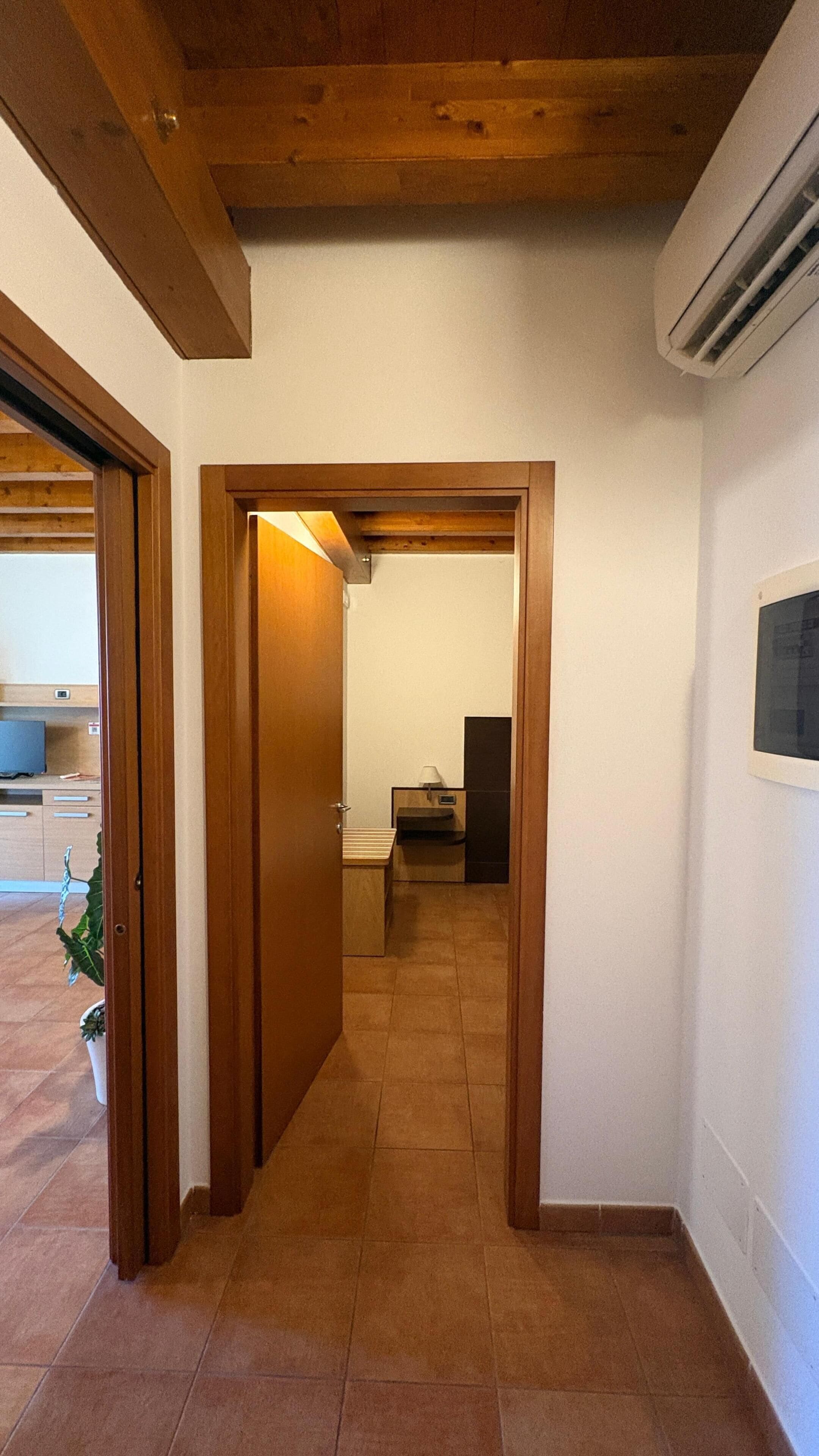 A hallway with wooden doors, a tiled floor, and a visible air conditioning unit.