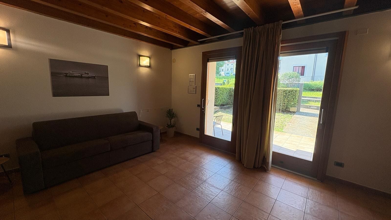 A room with a sofa, a potted plant, a sliding glass door, and a framed picture on the wall.
