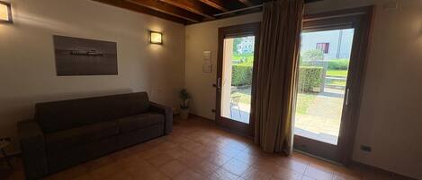 Ein Zimmer mit einer Couch, einer Topfpflanze, einer Schiebeglastür und einem gerahmten Bild an der Wand.