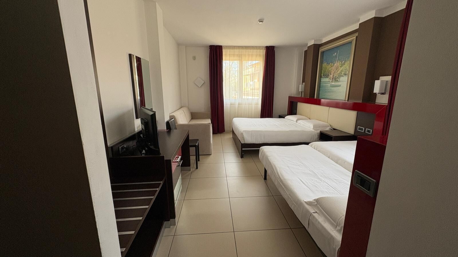 A hotel room with two beds, a desk, a TV, and a painting on the wall.