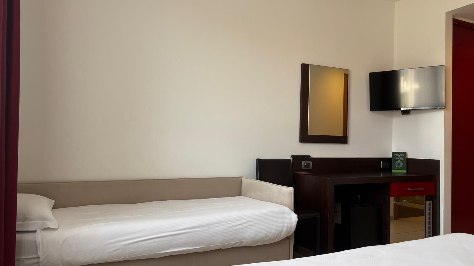 Een hotelkamer met een enkel bed, een bureau met een stoel, een flatscreen televisie aan de muur en een kleine tafel met een boek.